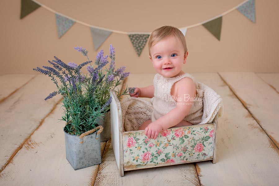 baby girl in vintage garden set, sat in a vintage floral crib with sage bunting and lavender tubs, on cream wooden floorboards