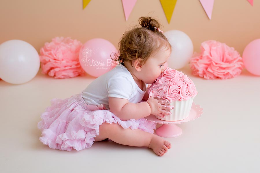 Baby girl eating a pink and white cake, wearing a pink tutu