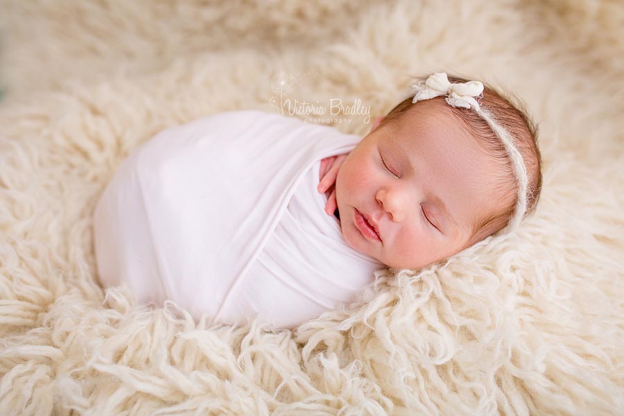 wrapped baby on cream flokati rug with a bow tie back and pale pink wrap