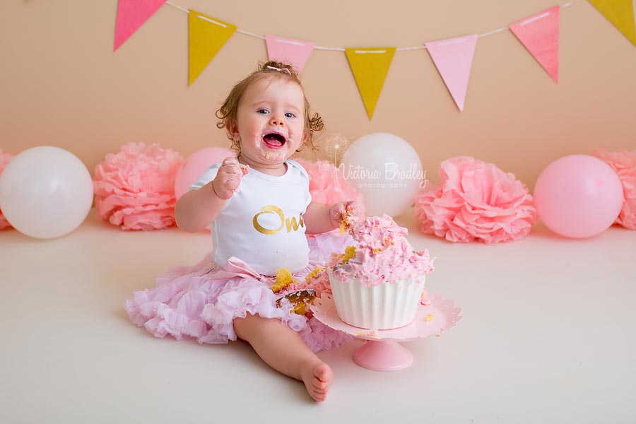 happy baby girl with birthday a pink and white cake for a cake smash