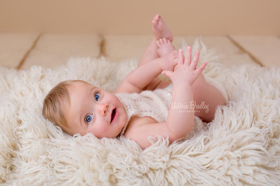 baby girl in alpaca yarn cream sitter romper lay on cream flokati rug