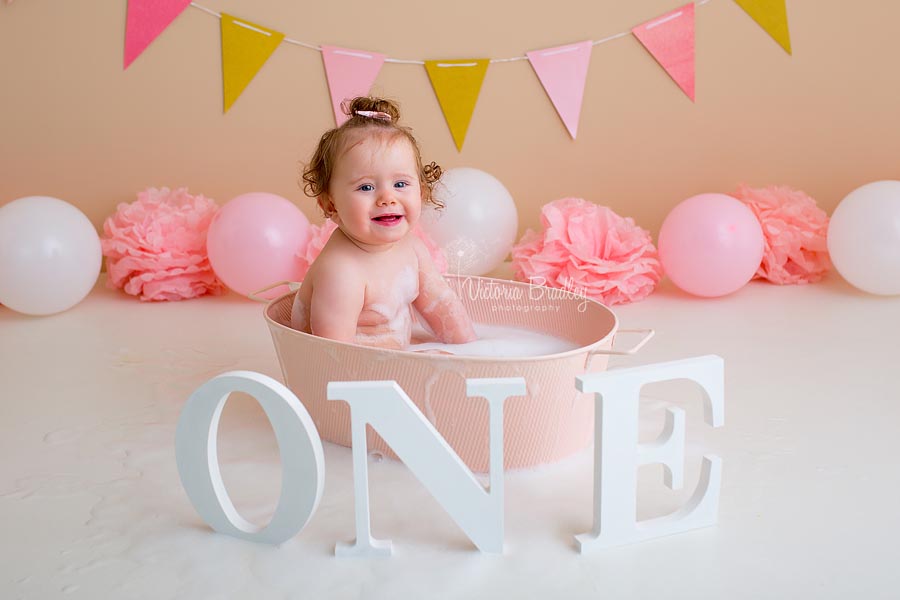 cake smash baby girl in pink bath tub with bubble and a white number one sign