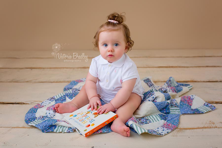 baby girl sat on top of a pretty blue quilt reading a happy birthday peter rabbit book