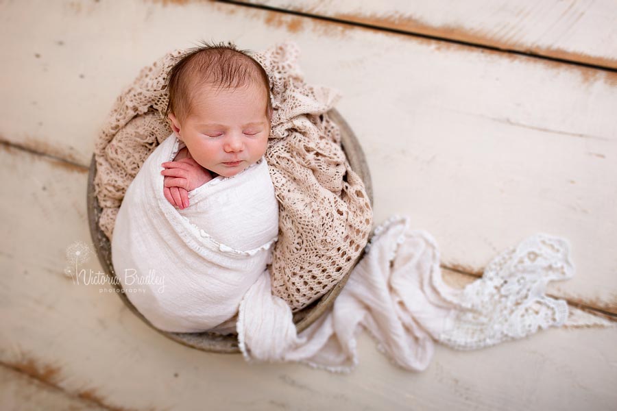 a wrapped baby with vintage lace basket stuffer in a metal bowl on cream wooden floor boards