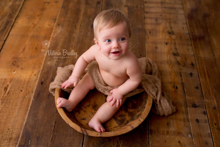 sitter baby girl sat in a wooden bowl on dark wood floor boards