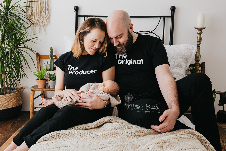 lifestyle photography with a newborn baby wrapped in a brown wrap held closely by the mother with the father sat close