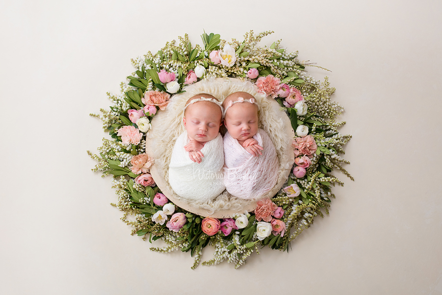 twin newborn babies in floral basket with cream and pink wraps on cream fluffy basket stuffer