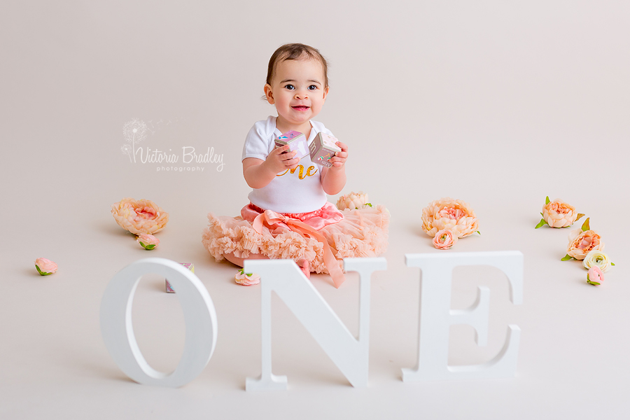 baby girl playing with blocks wearing a peach tutu and white top, with white wooden one letters