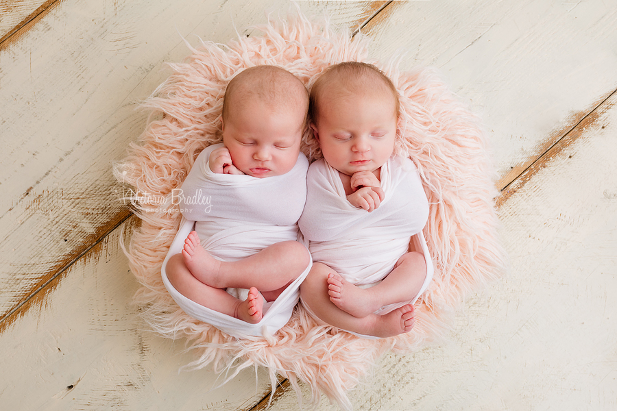twin newborn girls on pink fluffy basket stuffer with pink wraps