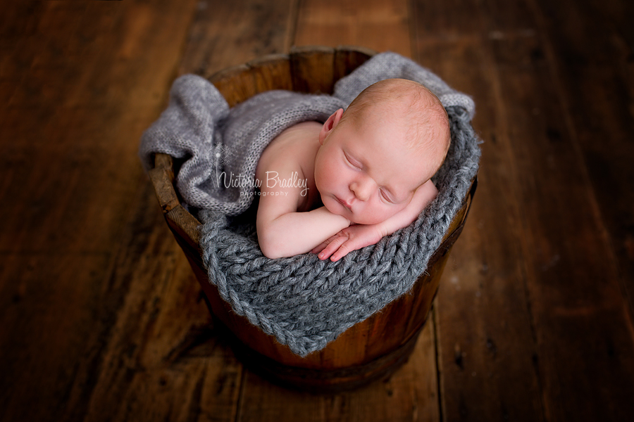 Newborn baby boy in a vintage wooden bucket with a grey knitted layer & grey wrap