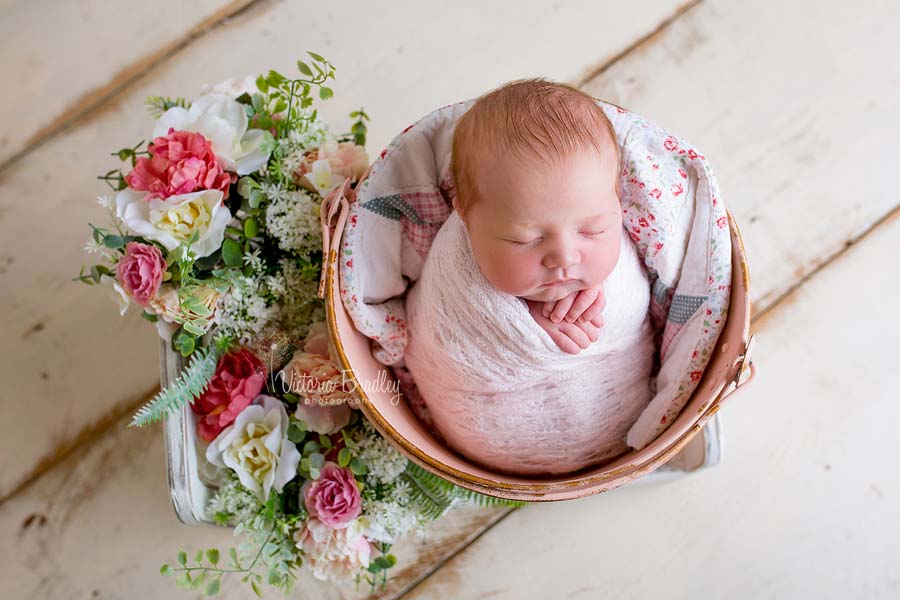 newborn baby girl in vintage pink bucket with a vintage quilt piece, with flowers