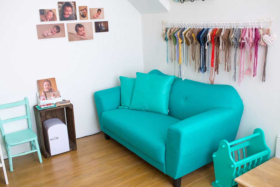 an aqua coloured couch on a wood floor in a white walled studio with photo blocks mounted on the wall