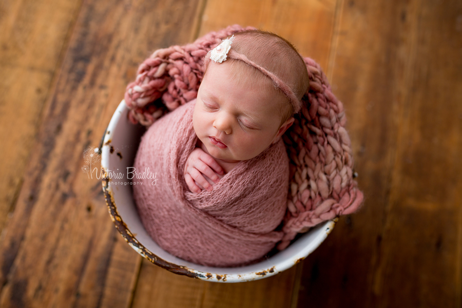 baby newborn in vintage white enamel bucket with rose pink blanket and knitted wrap