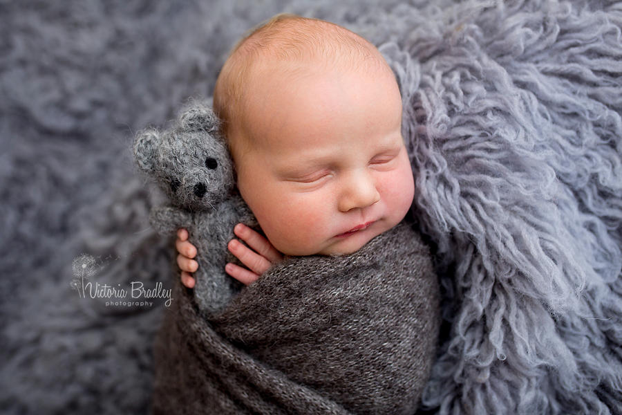 baby wrapped in grey with little grey teddy bear