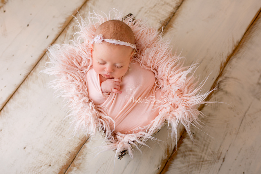 older newborn in peach wrap with peach fur stuffer in cream crate on cream wood floor