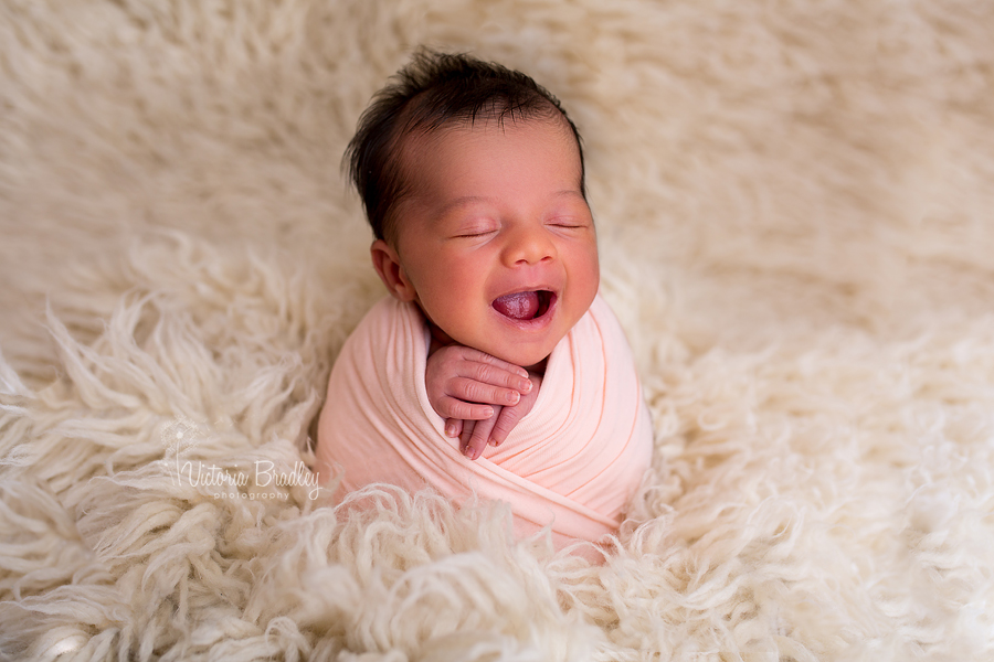 wrapped baby newborn in peach wrap on cream flokati rug