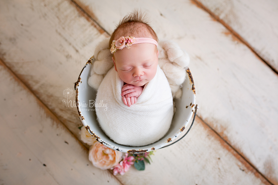 newborn wrapped in a cream knitted wrap in a white vintage pale with flowers on cream wooden floor boards