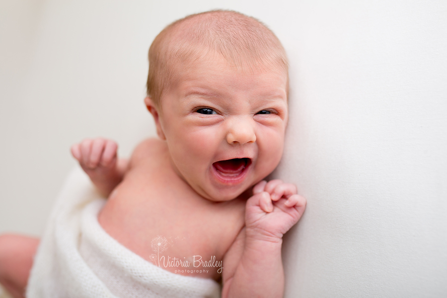 newborn laughing, smiling on cream backdrop with cream knitted wrap