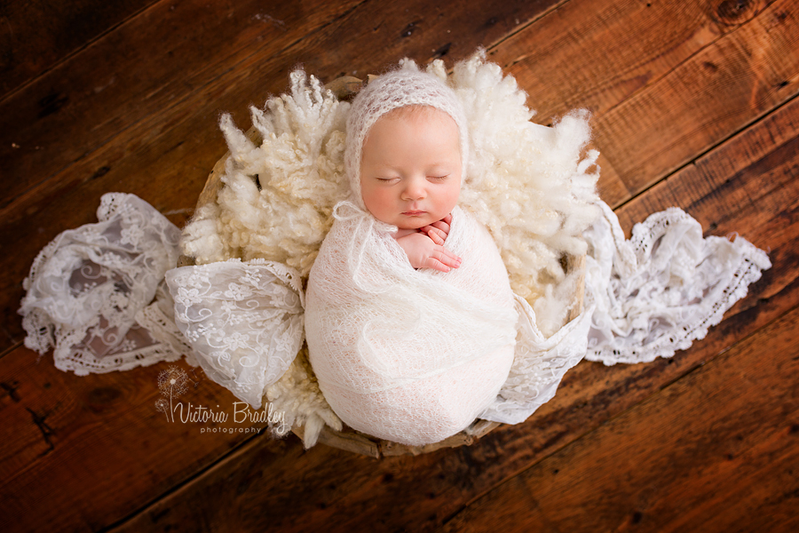 asleep baby wrapped in ivory knitted wrap on cream stuffer with driftwood bowl on dark wood planks