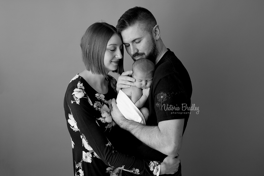 black and white image of a newborn baby with her mummy and daddy on a grey paper backdrop