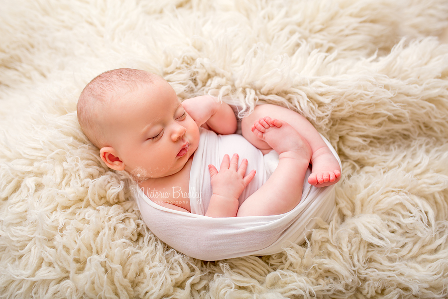 egg wrapped sleepy newborn in white wrap on cream flokati