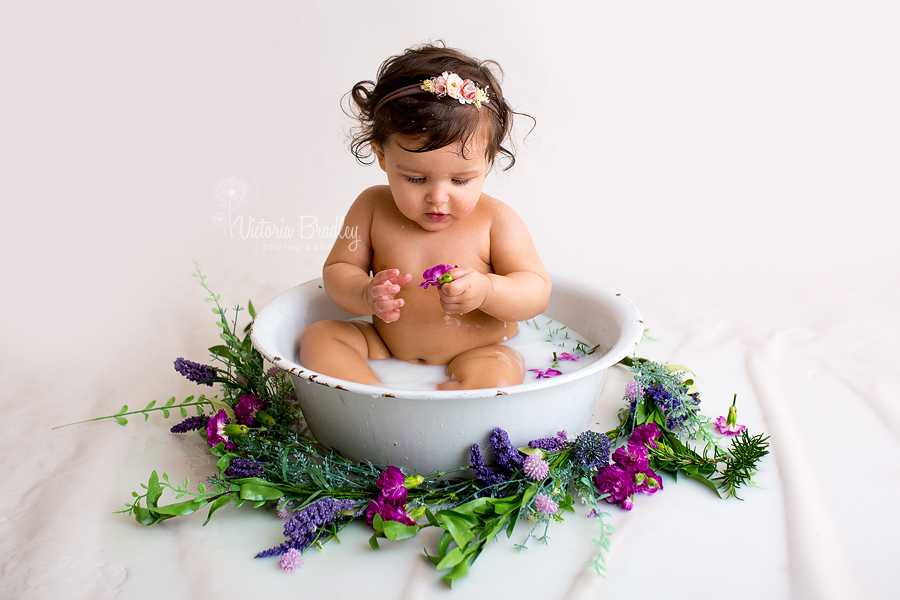 baby looking at a purple flower during a milk bath photography session in nottinghamshire