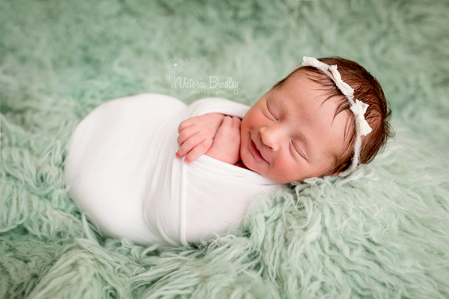 wrapped newborn baby on mint flokati