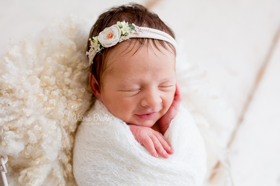 swaddled baby girl on curly basket stuffer with cream lace knit wrap with flower tieback