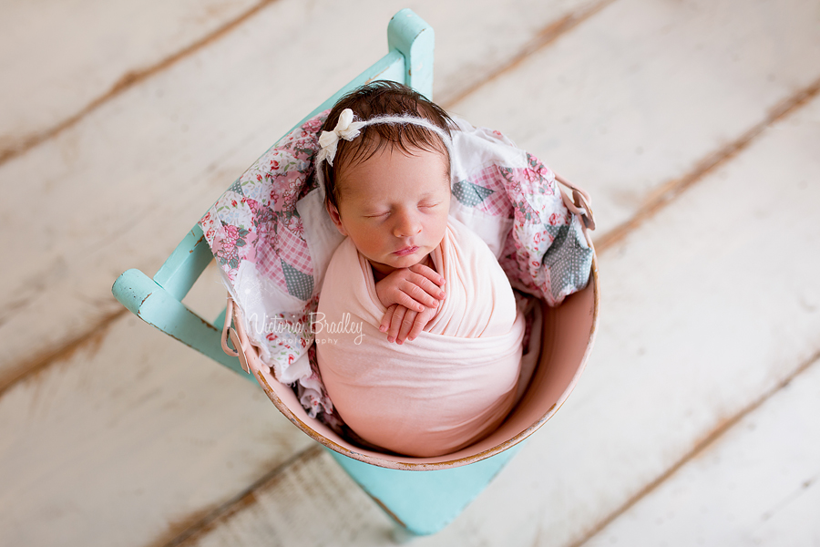 wrapped newborn in pink metal bucket with vintage quilt stuffer on a mint green chair