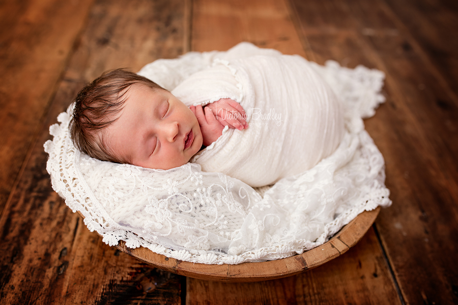 newborn baby girl with cream lace in a wooden bowl on a wooden floor