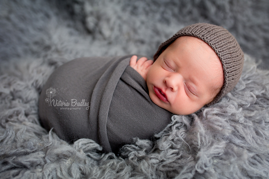 Gray flokati rug with wrapped newborn baby in a grey wrap & grey bonnet