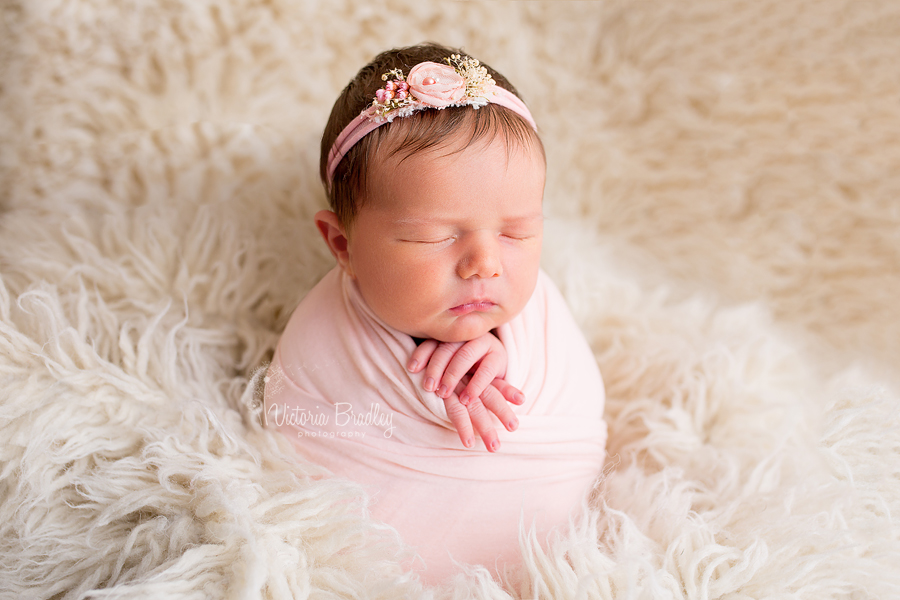 potato sack pose, peach wrap and peach tie back, newborn baby girl on cream flokati rug