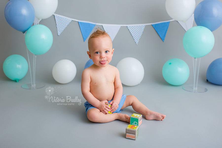 cake smash boy with grey backdrop, blue, mint and white balloons