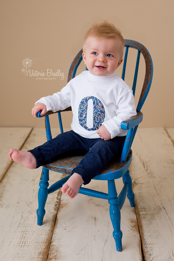 8 month old baby boy sat on a blue vintage chair.