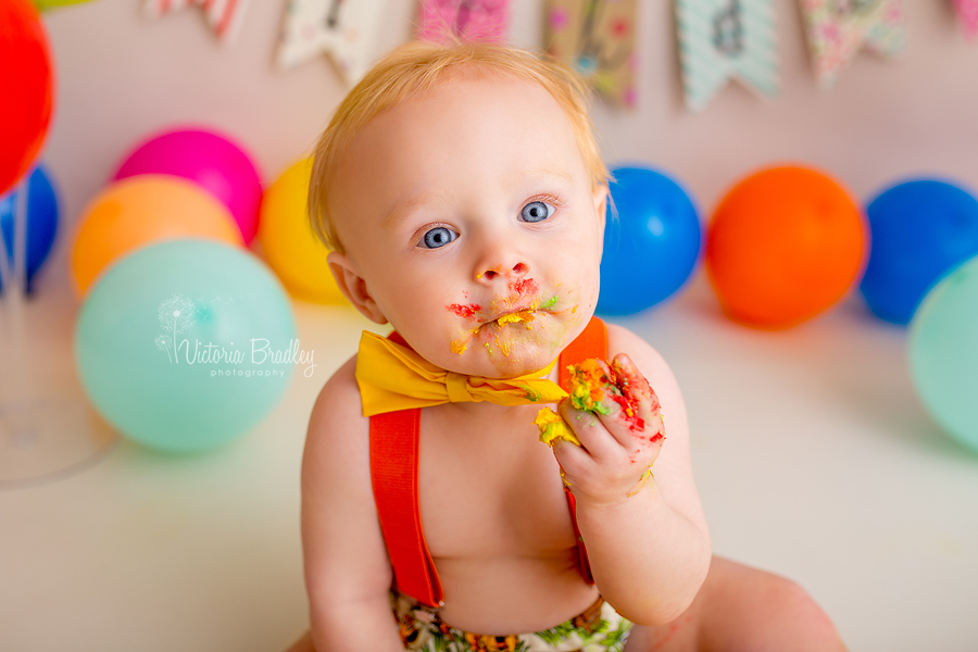 baby boy rainbow first birthday cake smash, holding cake, yellow bow tie