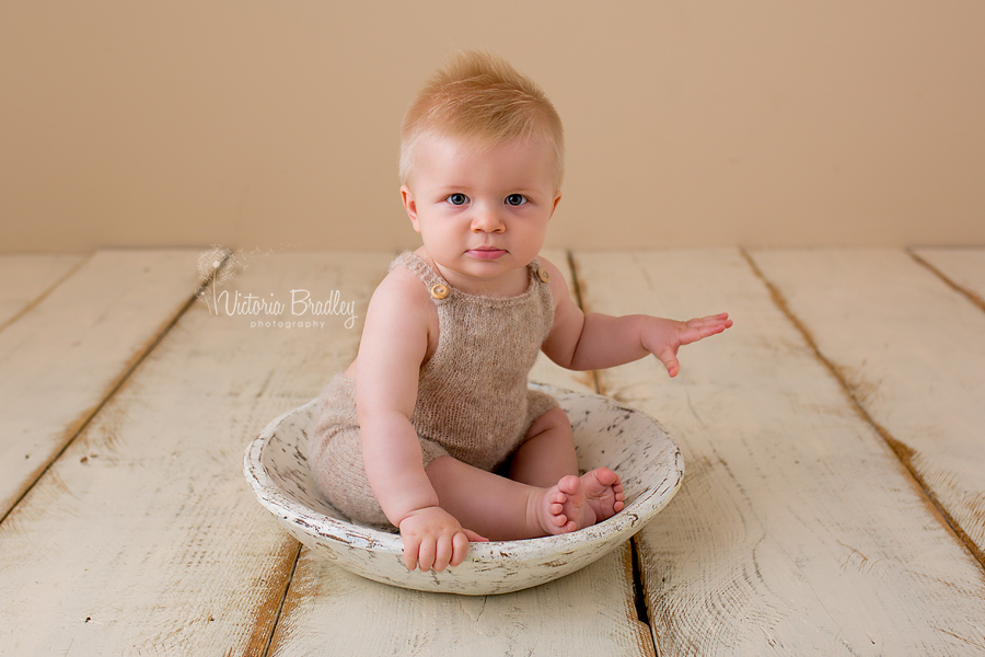 baby boy in knitted rompers in a white wooden bowl on cram wood floor boards