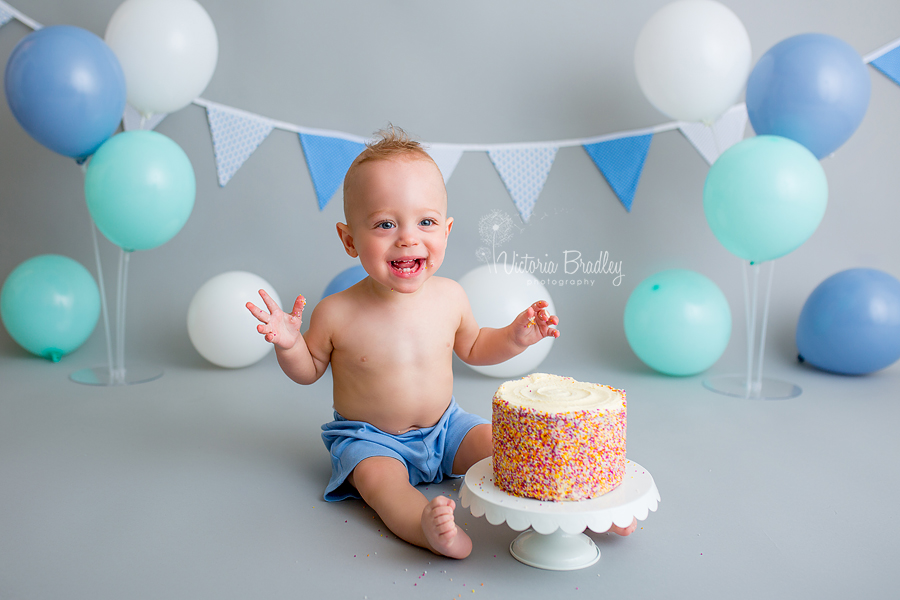 rainbow cake, cake smash, grey backdrop and blue and white balloons