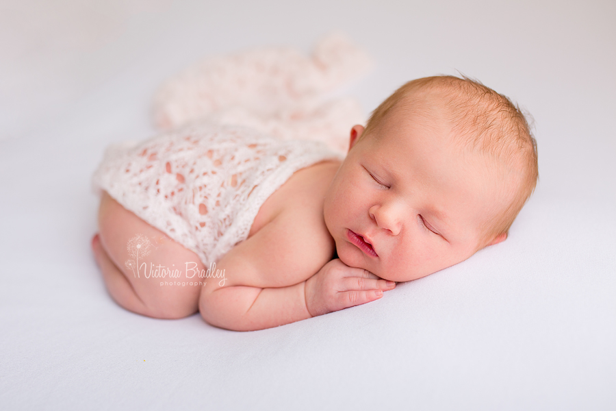 baby girl newborn on white blanket with pink lace knit wrap