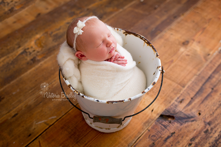 baby girl newborn baby in white enamel bucket on dark wood floor
