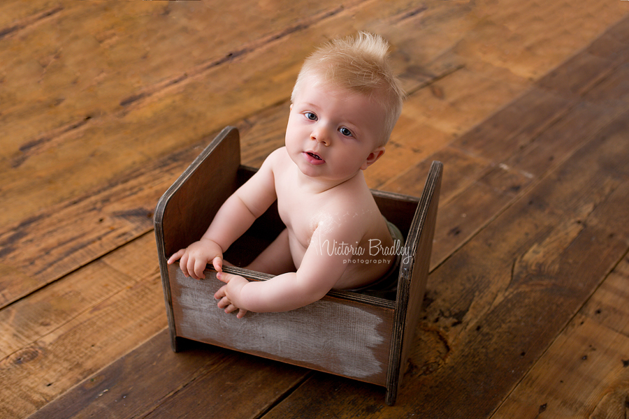 8 months old baby boy sat in brown crib with dark wood flooring