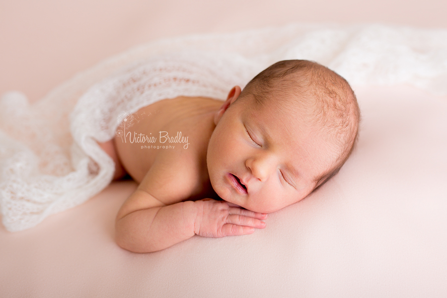 newborn baby girl on peach backdrop with white knitted lace wrap
