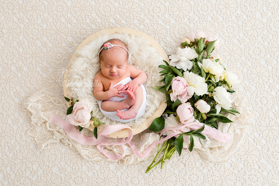 newborn baby in wooden bowl with flowers