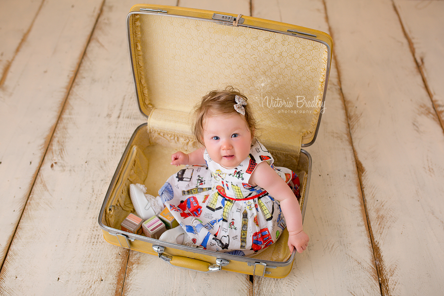 sitter baby girl in yellow suitcase with london print dress