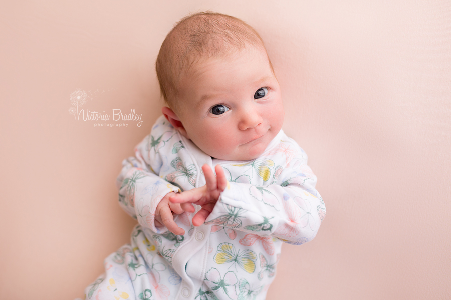 awake newborn girl on peach backdrop