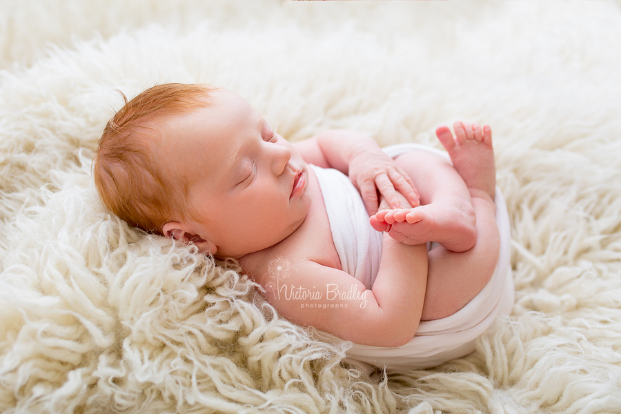 egg wrap newborn pose, on cream flokati with pale pink wrap