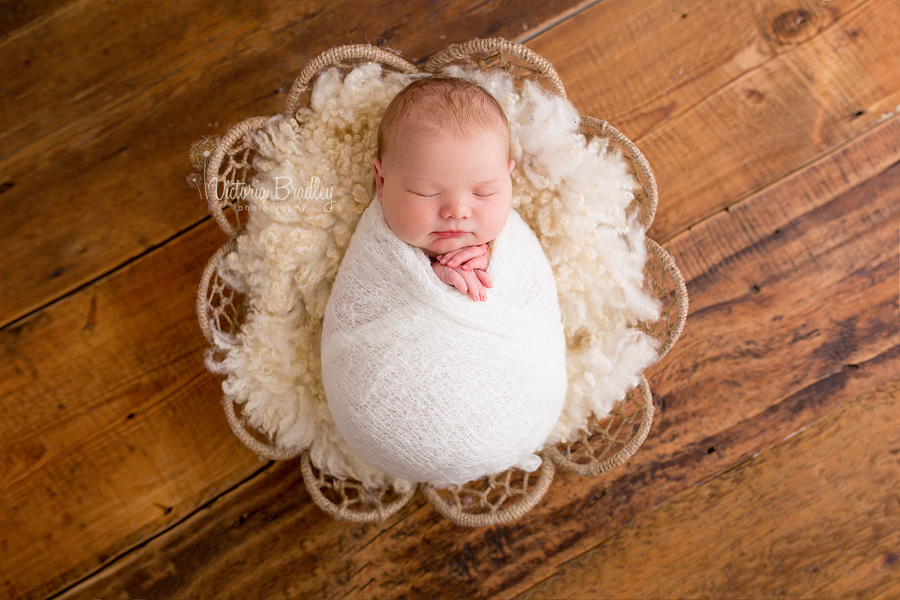 wrapped baby newborn in basket on dark wood floor