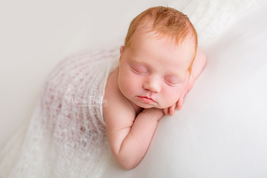 chin on hands pose, baby newborn girl on pale lemon backdrop with white lace knit wrap