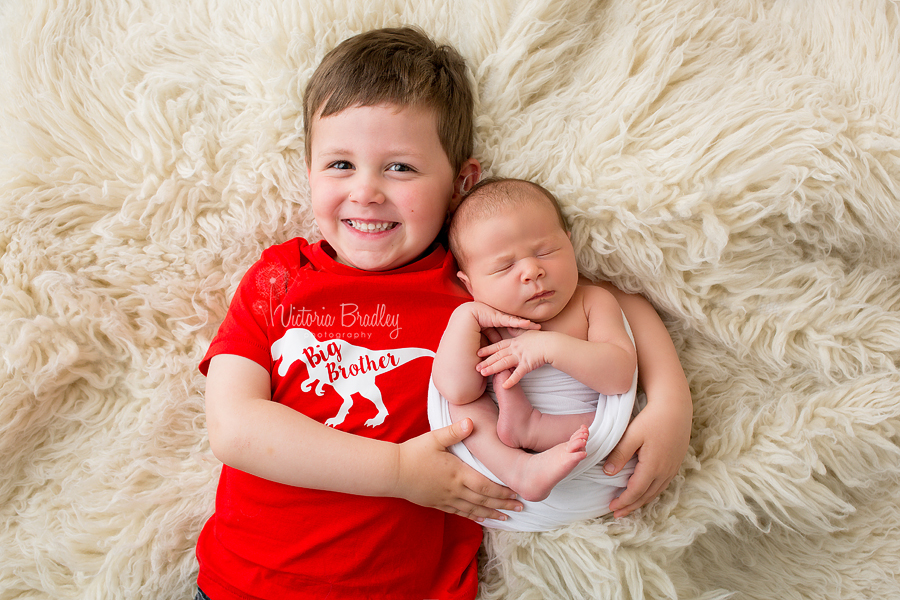 boy in red top cuddling newborn baby sister