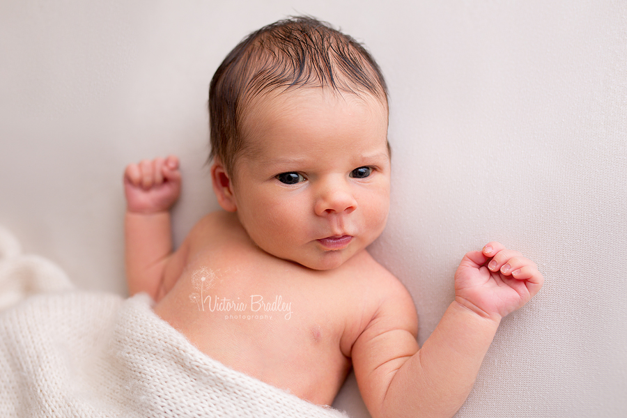 awake baby boy newborn on cream blanket