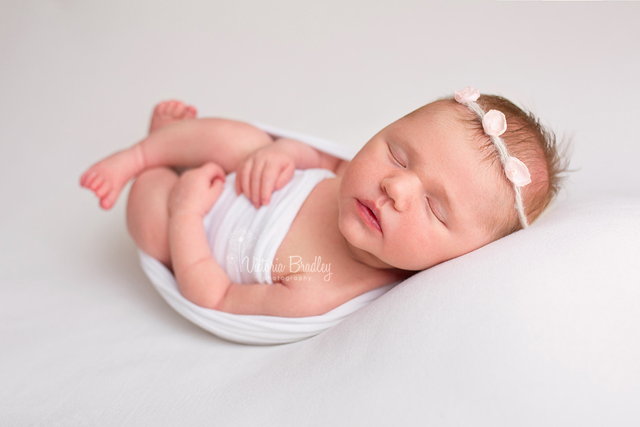 baby newborn girl on white backdrop with pink flower tie back hair band